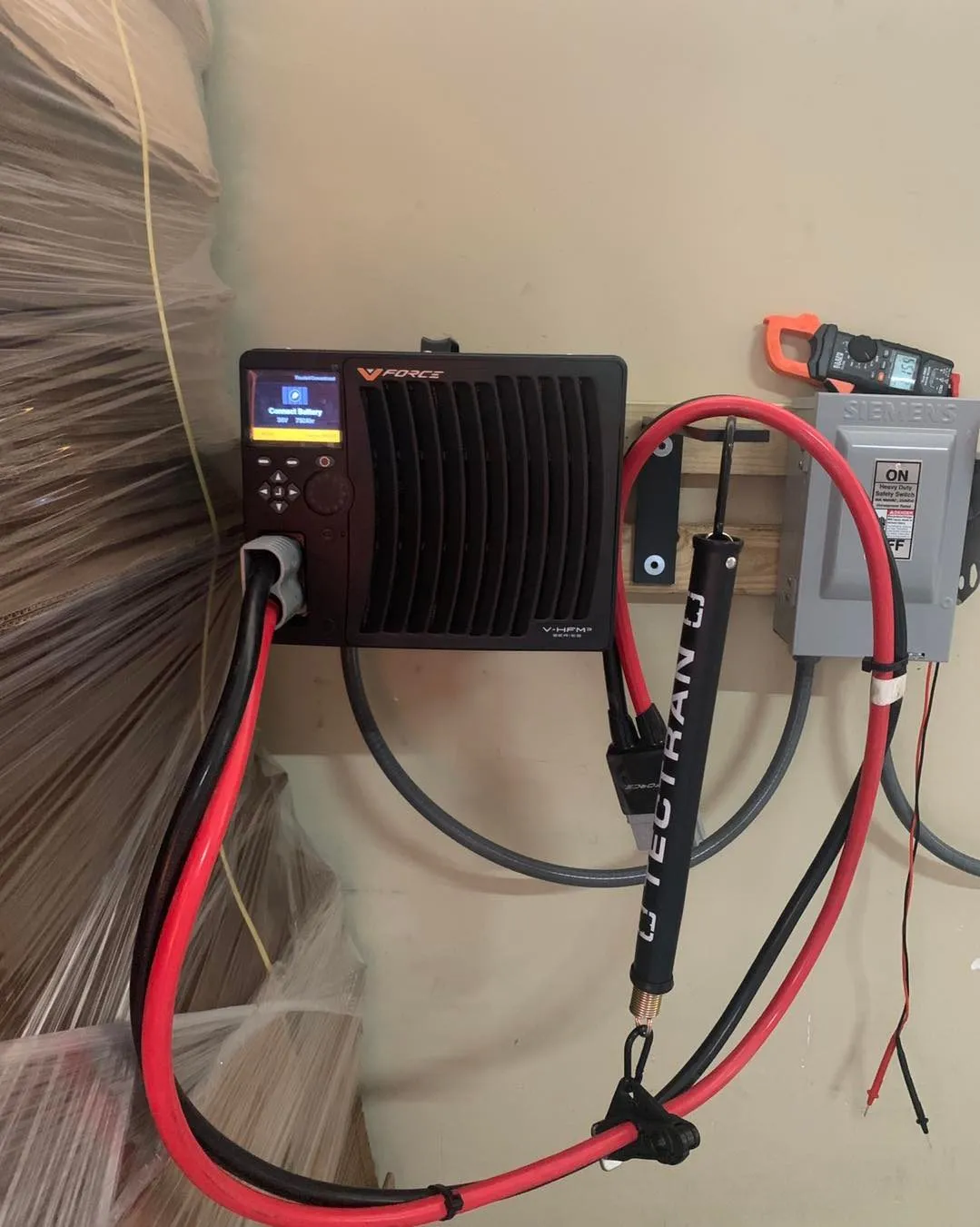 A backup power inverter mounted on a garage wall with neatly run red and black cables