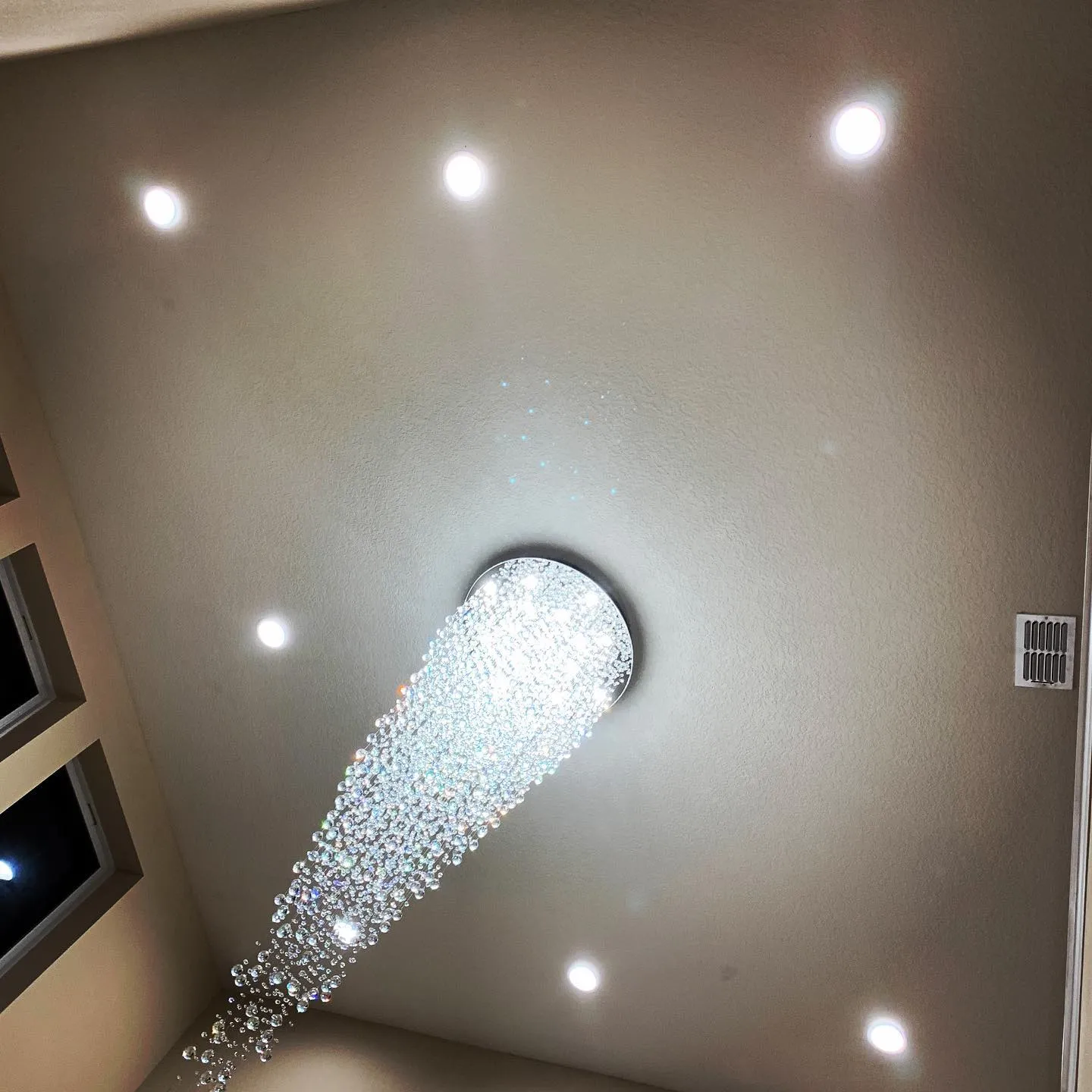 A crystal chandelier hanging from a vaulted ceiling with recessed lights around it