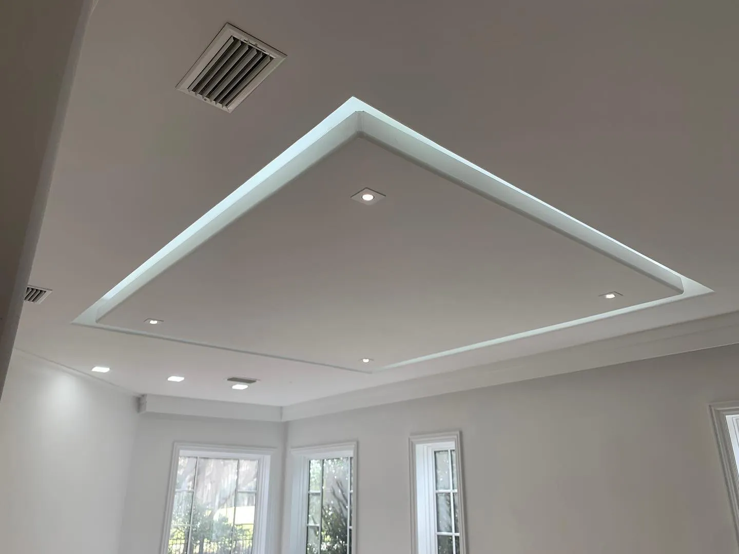 A living room ceiling with a recessed tray glowing with LED cove lighting and a ring of can lights