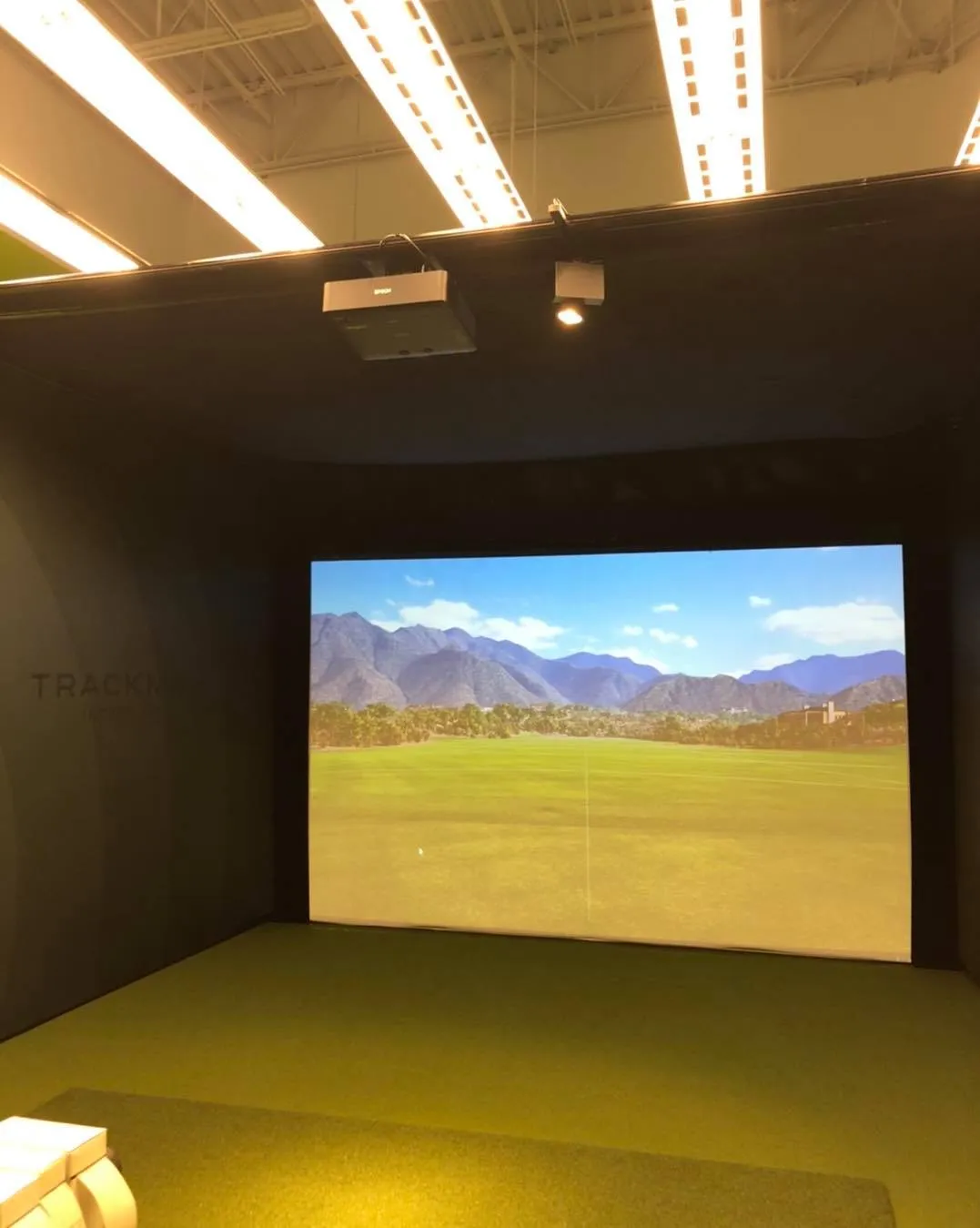 A home golf simulator room with a projection screen and overhead lighting