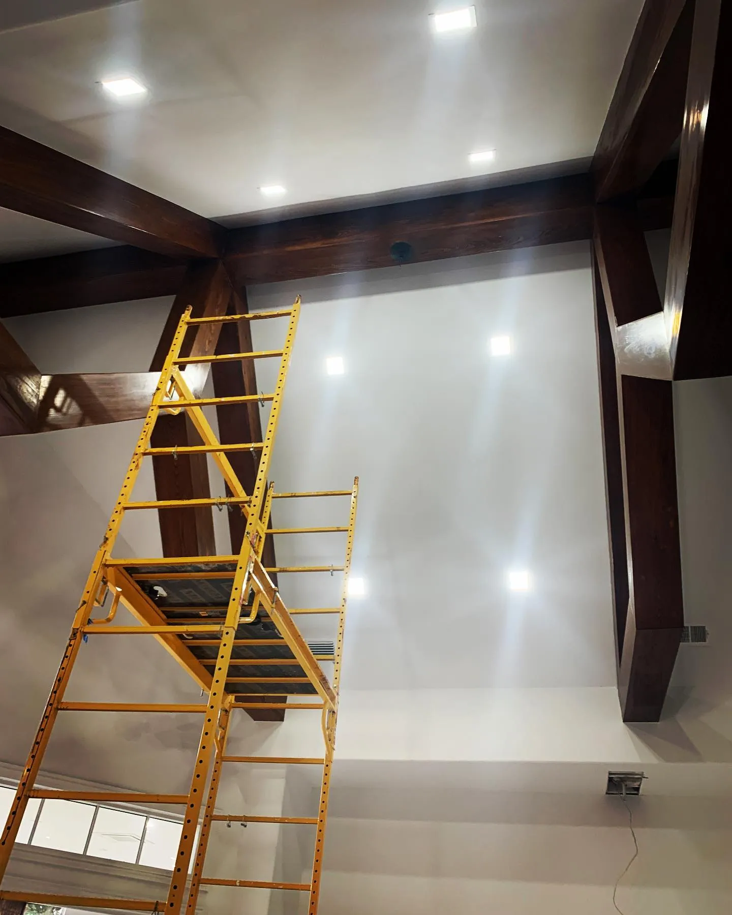 A two-story ceiling with new recessed lights, a work ladder still standing below
