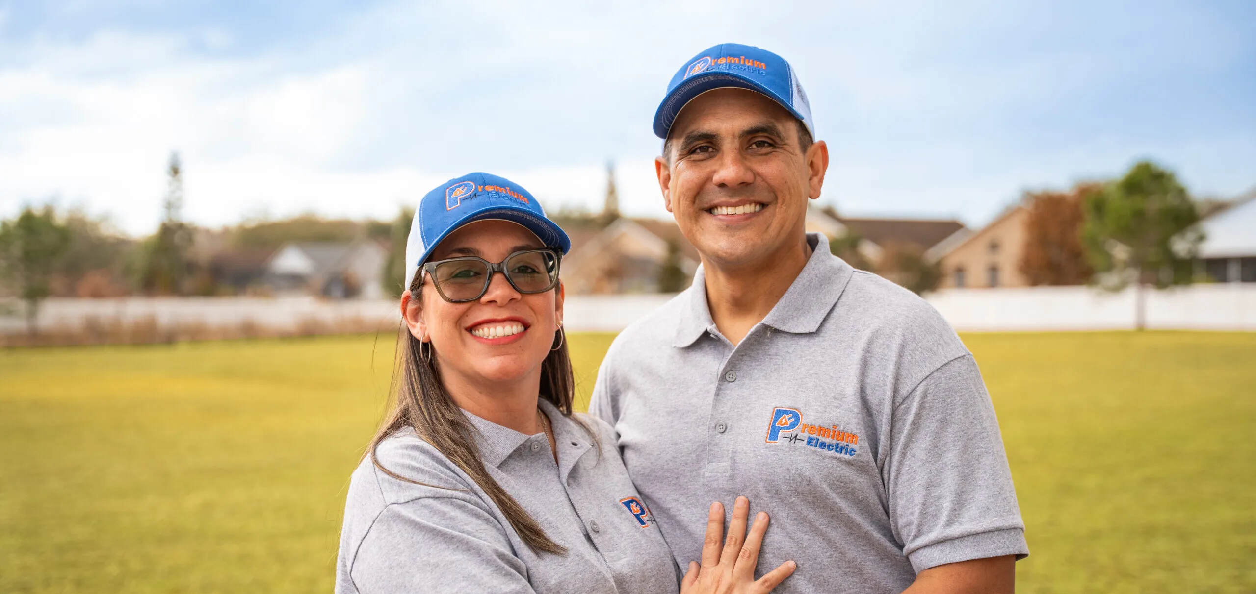 The owners of Premium Electric smiling together outdoors in company polos