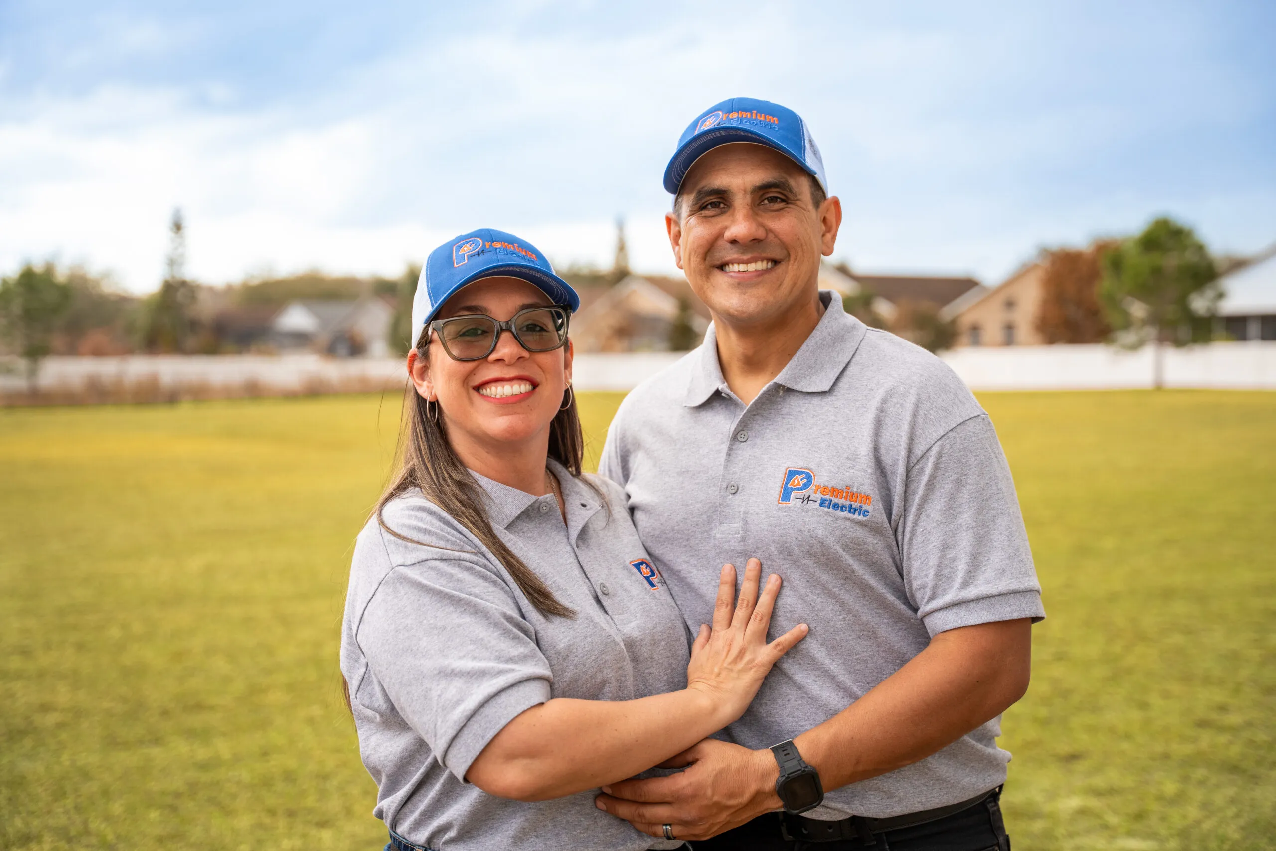 The owners of Premium Electric smiling together in company polos and caps
